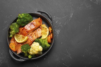Healthy baked fish salmon steaks, broccoli, cauliflower, carrot in cast iron casserole bowl black