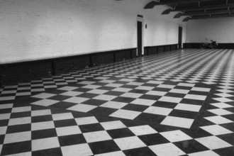 Chequered floor covering in front of a white house wall, behind it a vintage bicycle, black and