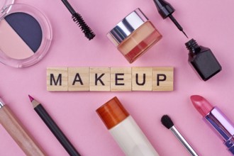 Close up of various female makeup accessories on pink background. Wooden cubes with text makeup
