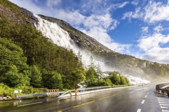 Summer cold day. The cascading Langfossen waterfall picturesquely intersects with the highway and