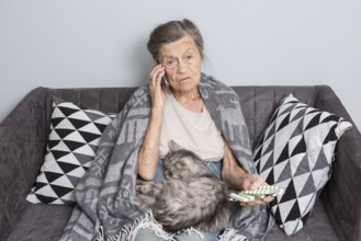 Sick senior woman taking medicine at home. Senior woman talking on mobile phone while looking at