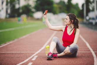 Young woman athlete at the stadium sporting lifestyle, sitting on the track, taking selfie photo on