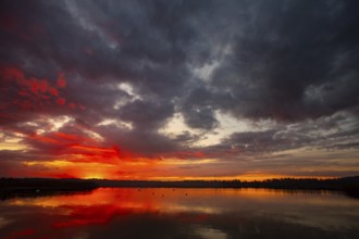 A truly stunning sunset over a calm and reflective lake showcases vibrant hues and dynamic clouds