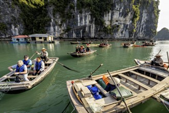 Tourists in boats enjoy a ride along a rocky shore, rowing boats for tourists in Halong Bay in