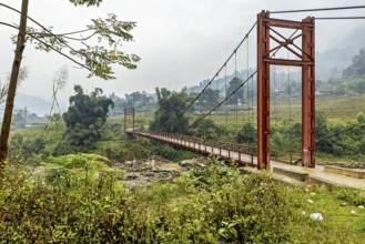 A red suspension bridge stretches across a green valley under an overcast sky, A bridge over a