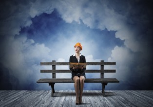 Beautiful woman architect sitting on wooden bench. Young technician specialist in orange safety