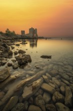 Castle ruins at dawn. Bay on the Mediterranean Sea with calm water at sunrise. Reflection of the