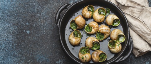 Escargots de Bourgogne Snails with Garlic Butter and Parsley in black cast iron pan on rustic stone