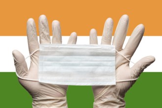 Paramedic holding face mask in two hands in white medical gloves on background flag of India.