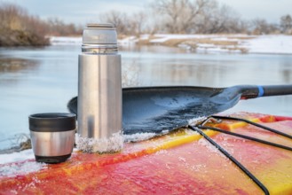 Winter kayaking in Colorado - thermos bottle with hot tea on the icy deck of a red whitewater kayak