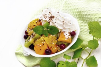 Fruit salad with orange, kiwi, cranberries and baked pumpkin, whipped cream, sprinkled with