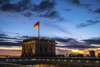 The Berlin Reichstag in the evening sky with the flag of Germany and clouds in the background. The