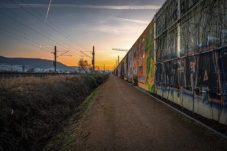 A path along a graffiti-covered wall at sunset, with rails and urban atmosphere, Jena, Thuringia,