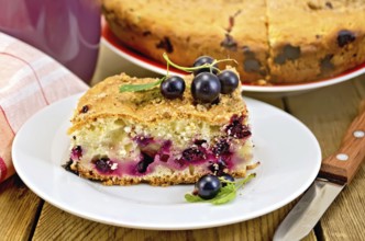 Sweet piece of cake with black currant, napkin, cup, knife on background wooden plank