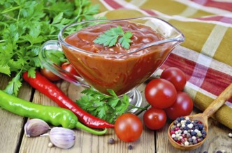 Ketchup in a glass gravy boat, tomatoes, parsley, hot pepper, garlic, napkin on a wooden boards