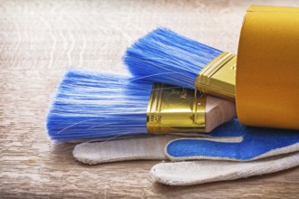 Two paint brushes in roll of duct tape and working gloves on wooden board