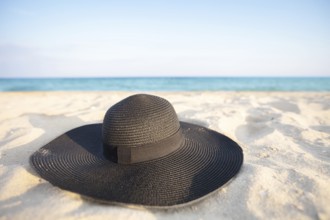 Black hat on a background of the sea. Beach accessory on white sand. Straw panama on the background