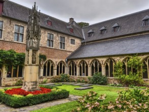 Small monastery courtyard with well-tended garden, Gothic arches and a central stone sculpture,