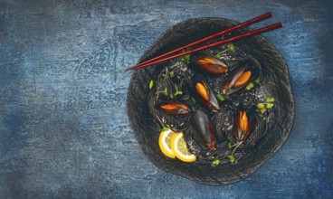 Spaghetti with black squid, black pasta, with boiled mussels, on a black plate, with parsley and