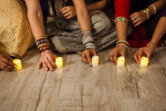 Women's hands holding lighted candles, sitting on floor. Indian holiday Diwali traditions. Closeup