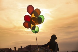Pretty girl with big colorful balloons walking on the hills near the town. Focus on balloons