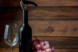 Wine bottle with corkscrew, empty wineglass and bunch of grapes on wooden background, ready for