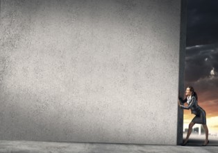 Young businesswoman making effort to move cement wall