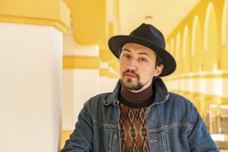 Portrait of a stylish handsome young man with a scarf outdoors. A serious man wearing a hat and a