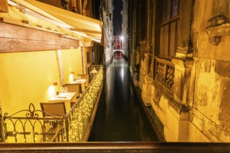 Restaurant tables on a balcony above a canal, night shot, Venice, Italy