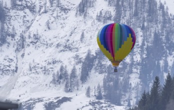 Colourful rainbow coloured hot air balloon, balloon rises, snowy landscape