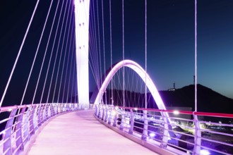 Pedestrian perspective on a suspension bridge illuminated with purple lights at night, in