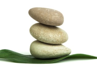 Stacked stones on base of green leafs. White isolated studio shot