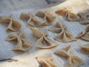 Fresh raw homemade whole-grain pasta in the shape of a bow, Farfalle, on a wooden board