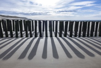 Old, weathered volleyball net on the beach in front of the dunes with sea and blue sky in the