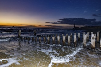 Wooden piles, groyne, in the sea at sunset with stormy sky, Groede, Zeeland, Netherlands