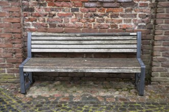 Empty wooden bench with metal frame sits against a weathered brick wall, inviting contemplation and