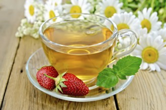 Tea with strawberries in a glass cup, a bouquet of daisies on a background of wooden boards