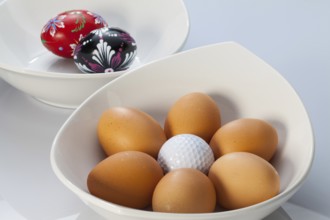 Two white ceramics bowls, easter eggs and golf balls