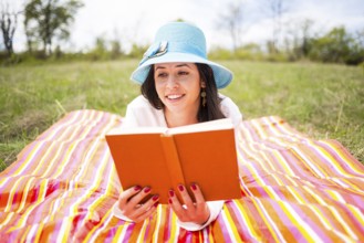 Attractive smiling young woman dressed casually reads orange old book lying down on a colourful
