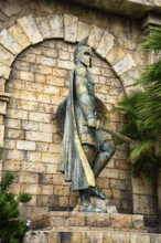 Close-up of an ancient statue with helmet and shield amidst stonework and greenery, palms, city,