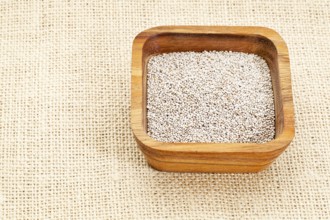 White chia seeds in square wooden bowl against burlap canvas