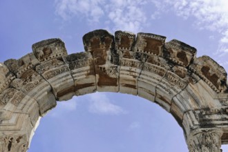 Ancient stone arch with decorative details against a blue sky, Turkey, Ephesus: Tourists encounter