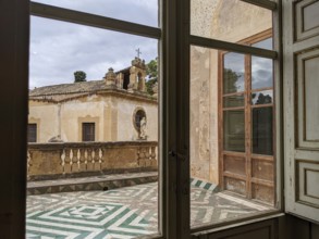 A window view of a historic terrace with patterned floor tiles and vintage architectural elements,