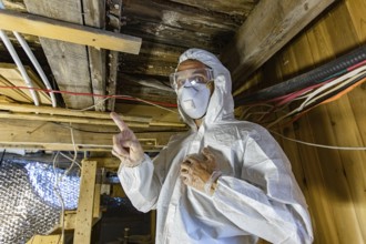 An indoor environmental quality assessor is viewed up-close, working beneath timber floor joists