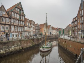 Foggy canal scene with half-timbered houses and a sailing boat, enhanced by the historical
