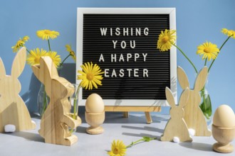 WISHING YOU A HAPPY EASTER text on letter board with bunny wooden figures and fresh flowers. Easter