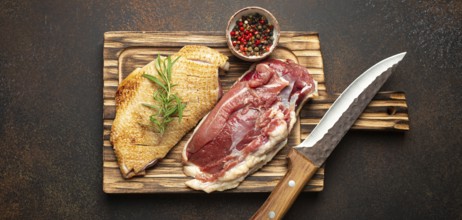 Two raw uncooked duck breast fillets with skin, seasoned with salt, pepper, rosemary top view on