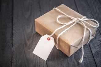 Gift box, wrapped in brown vintage paper and tied with white flax string, on an old black wooden