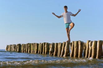 A young man stands on the breakwater, wooden breakwater, breakwater in the sea for protection from