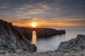 A view of the landmark stone arch of Pont d'en Gil on Menorca Island at sunset